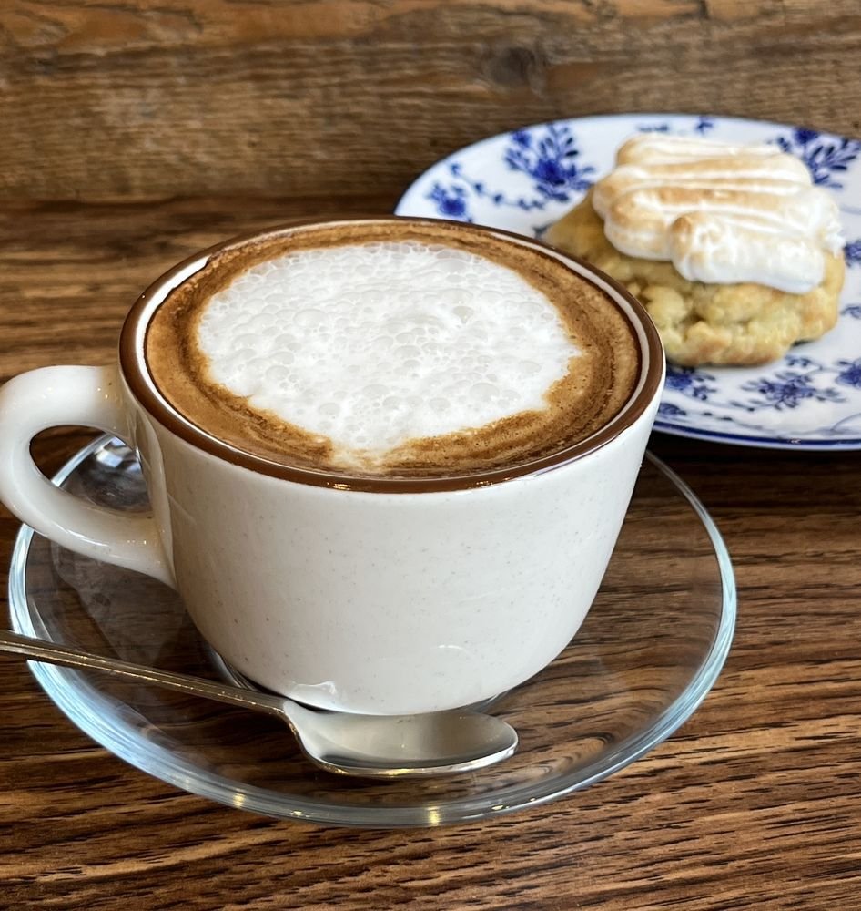 Cappuccino dans une tasse blanche avec un cookie coiffé de meringue sur une assiette fleurie bleue.