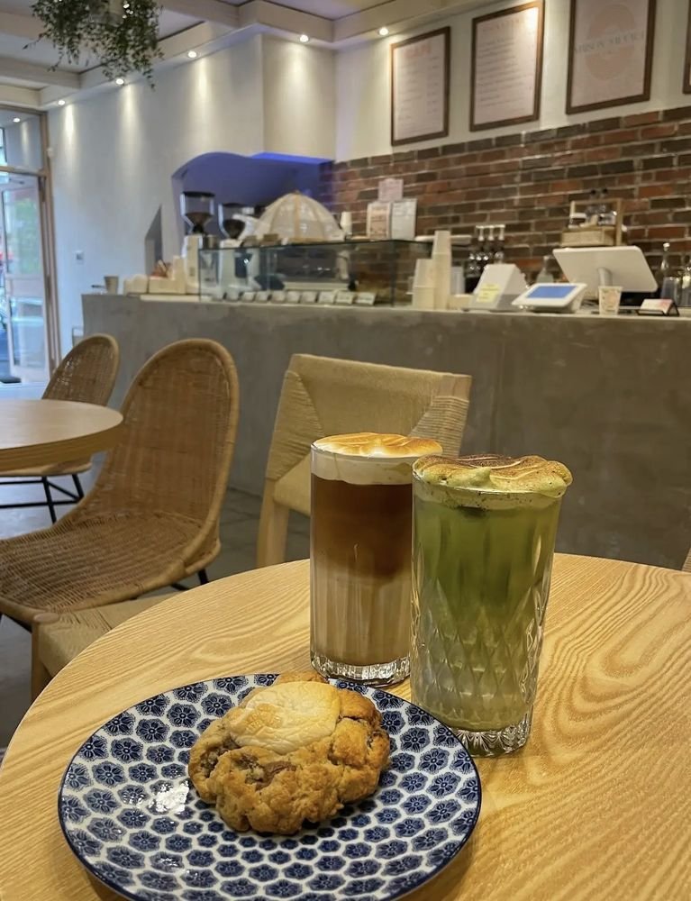 Intérieur chaleureux de Maison Sauvage Café : fauteuils en rotin, mur de brique et cloud lattes coiffés de meringue toastée.