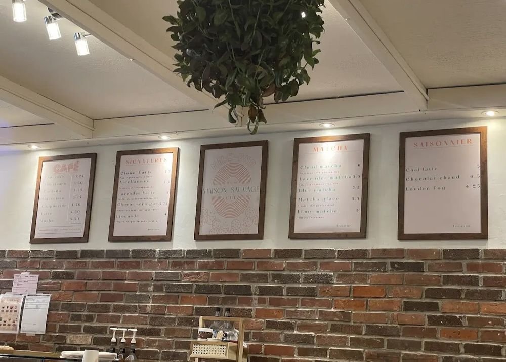 Les tableaux du menu de Maison Sauvage encadrés sur le mur de brique : Café, Signatures, Matcha, Saisonnier.