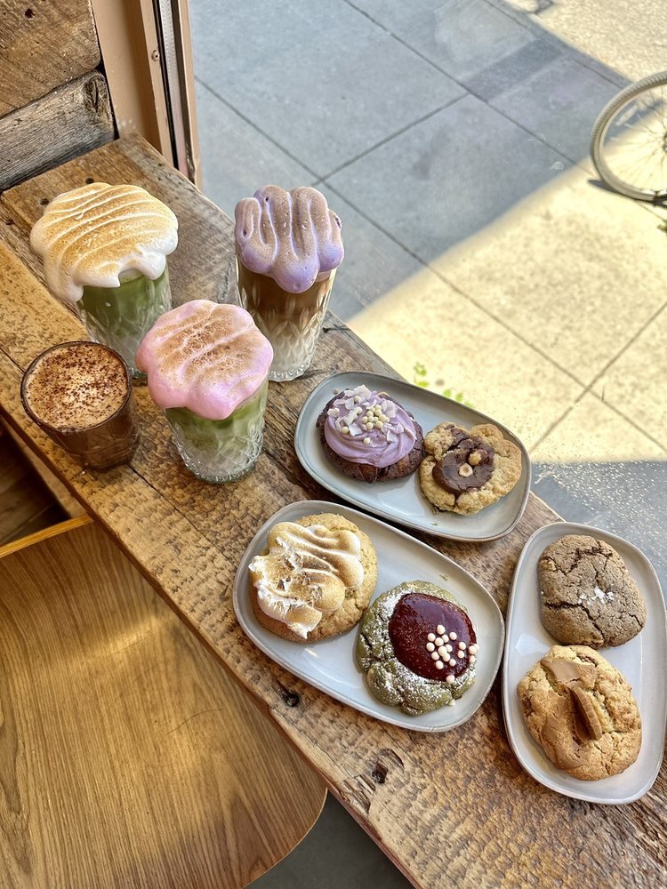 Cloud lattes et cookies gourmands alignés sur le rebord de fenêtre en bois de Maison Sauvage, lumière du matin sur la rue Bernard.